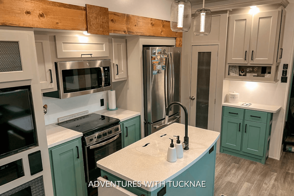 Our completed RV kitchen remodel. The trim has been replaced, the upper cabinets are painted light grey, and the lower cabinets and island are painted green. 