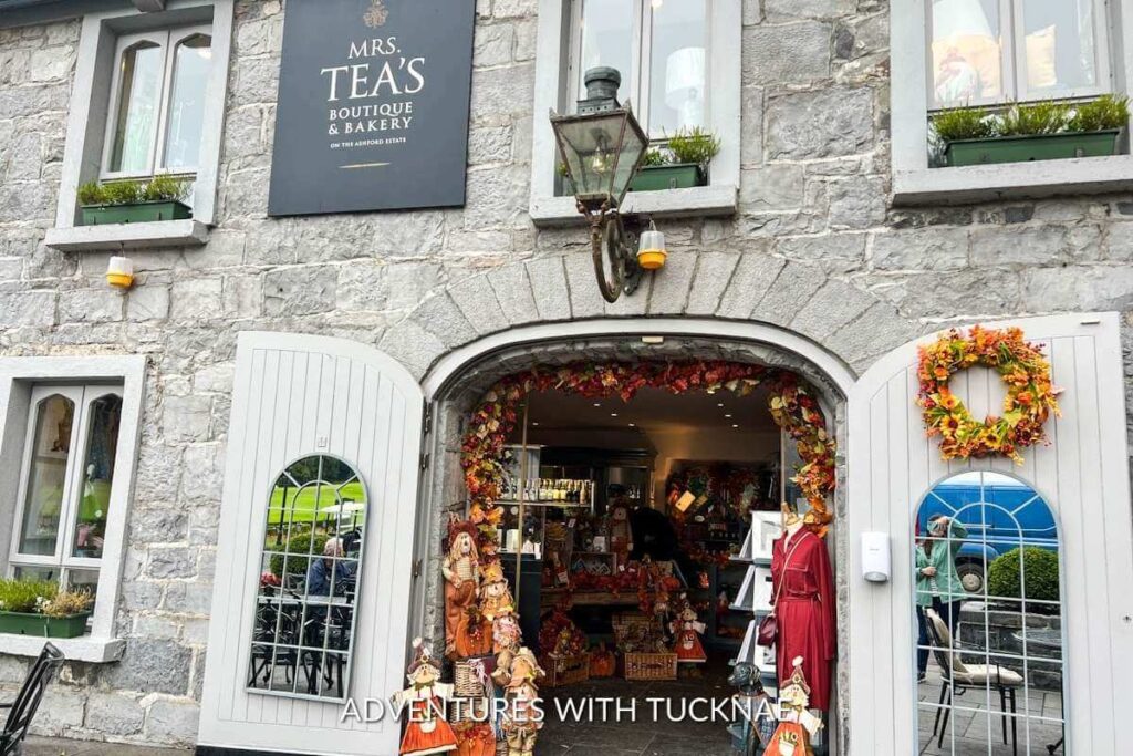 Standing outside of Mrs. Tea's Boutique at Ashford Castle. There are fall decorations around the entryway, and the sign above the door reads, "Mrs. Tea's Boutique & Bakery"