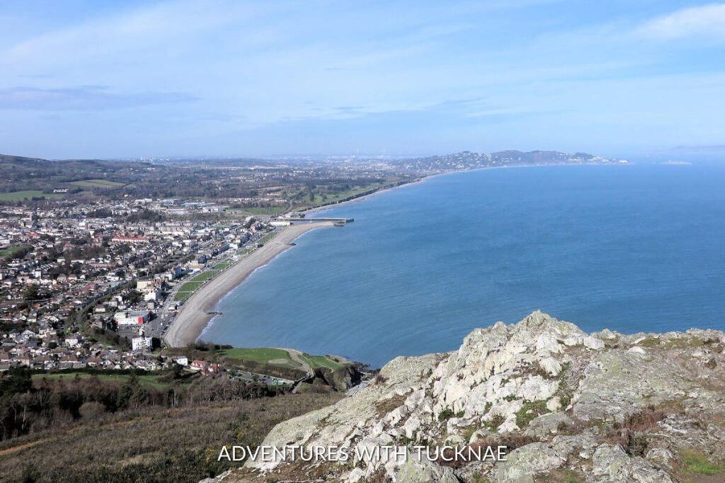 A high view of Bray, Ireland, from a vantage point. The town is far below along the edge of the ocean, with a sandy beach separating them. 