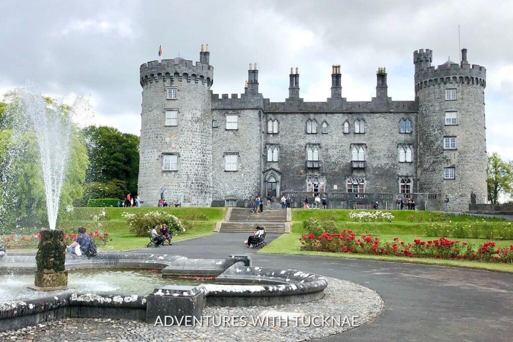 A beautiful view of Kilkenny Castle in Kilkenny, Ireland. The castle is surrounded by gorgeous gardens with a water fountain. 
