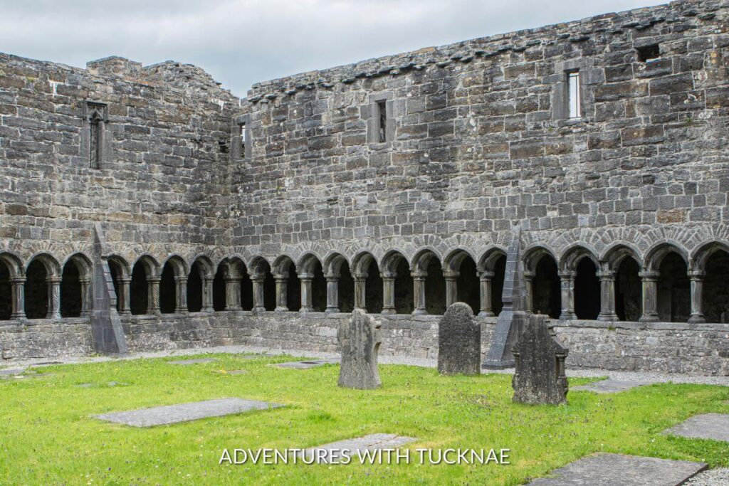 Inside the courtyard of Sligo Abbey in Ireland. There are headstones in the graveyard, surrounded by stone walls with many small archways.