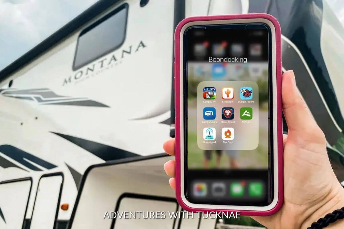 A pink phone is being held up with an RV in the background. The phone is showing a folder of apps labeled boondocking.