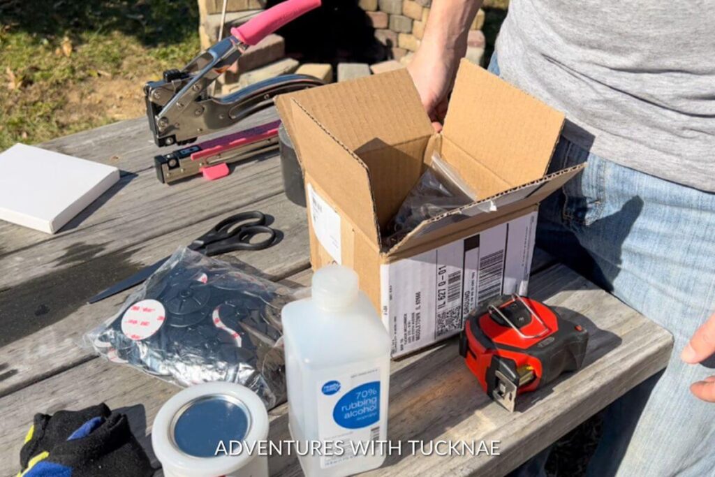 A picnic table covered in all of the supplies we used for our DIY RV skirting, including a pink crop-a-dile, rubbing alcohol, a tape measure, adhesive snaps, and more