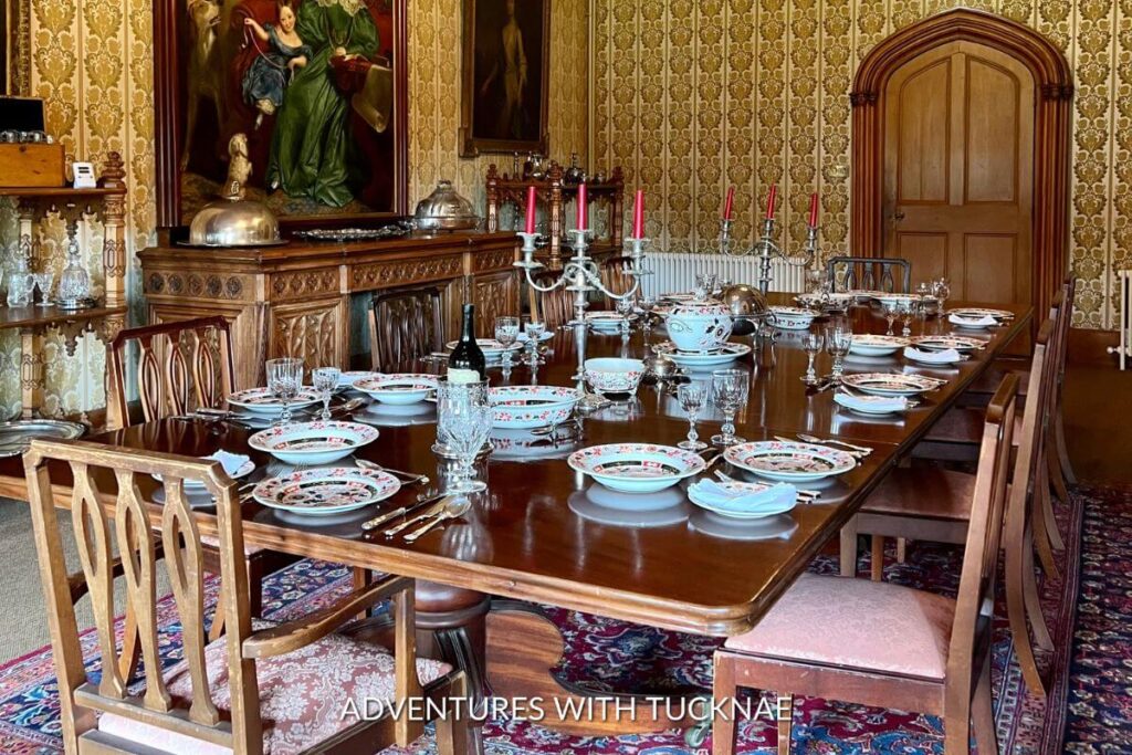 Castle interior featuring the dining table fully set with cups, plates, bowls, and silverware. There is a family portrait hanging on the wall, and the room is stylishly decorated to reflect the history of the castle. 