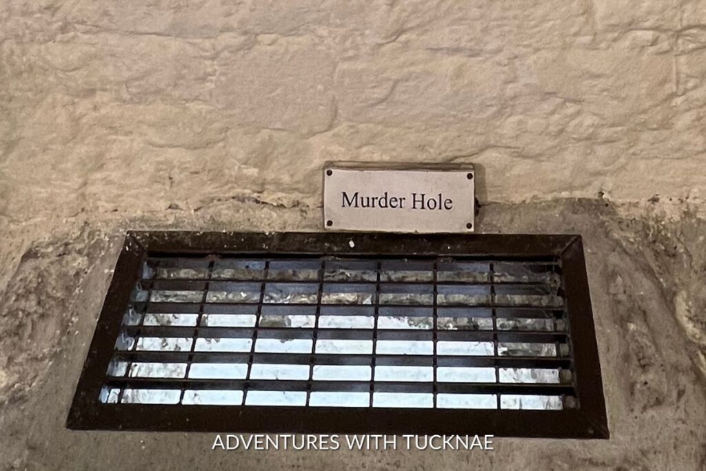 Murder Hole in the castle. There is a grate covering the opening, and a sign that reads "murder hole"