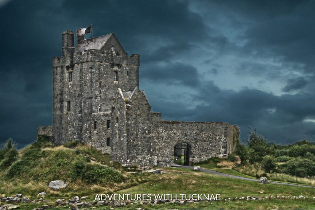 An ominous photo of Oranmore Castle in Galway Ireland. The sky is dark and looming nad the castle is shadowed . There is a flag flying on the castle and the ground surrounding it is bright green