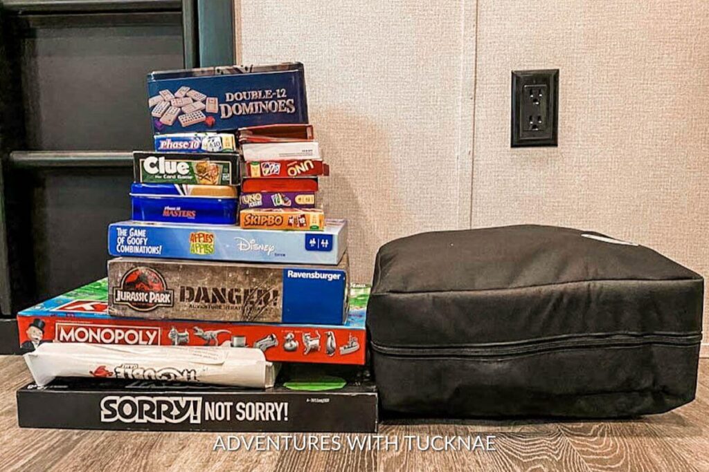 A tall stack of board game boxes sitting on the floor next to the Mod game organizer in our RV. This shows how many games fit into the organizer to save space.