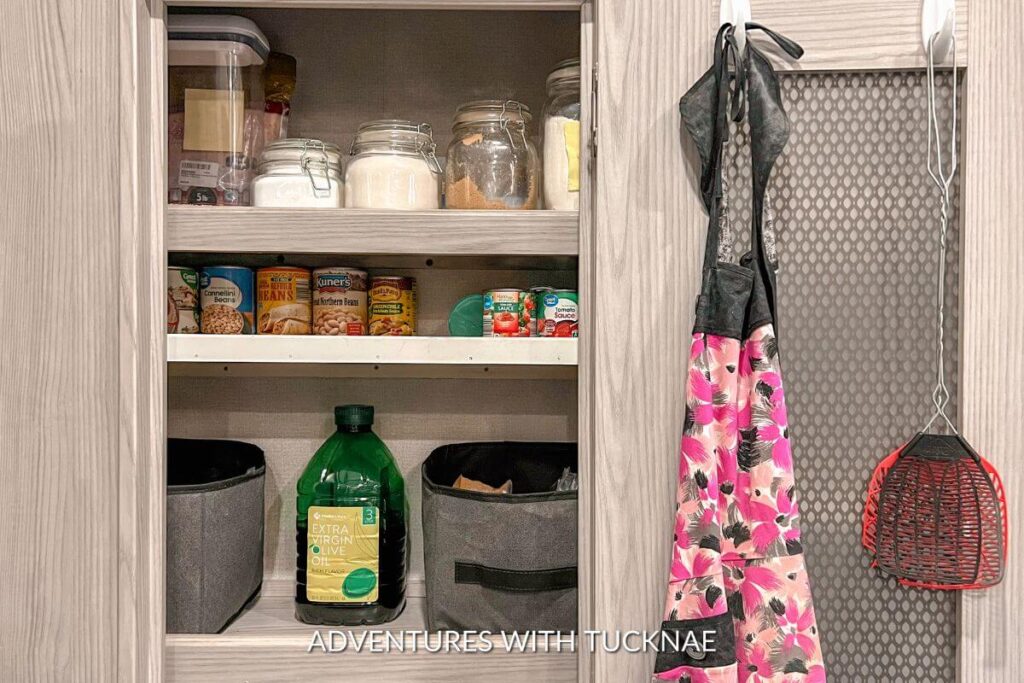 RV pantry organization with command hooks hanging fly swatters and an apron. There are pantry goods on the shelves. 