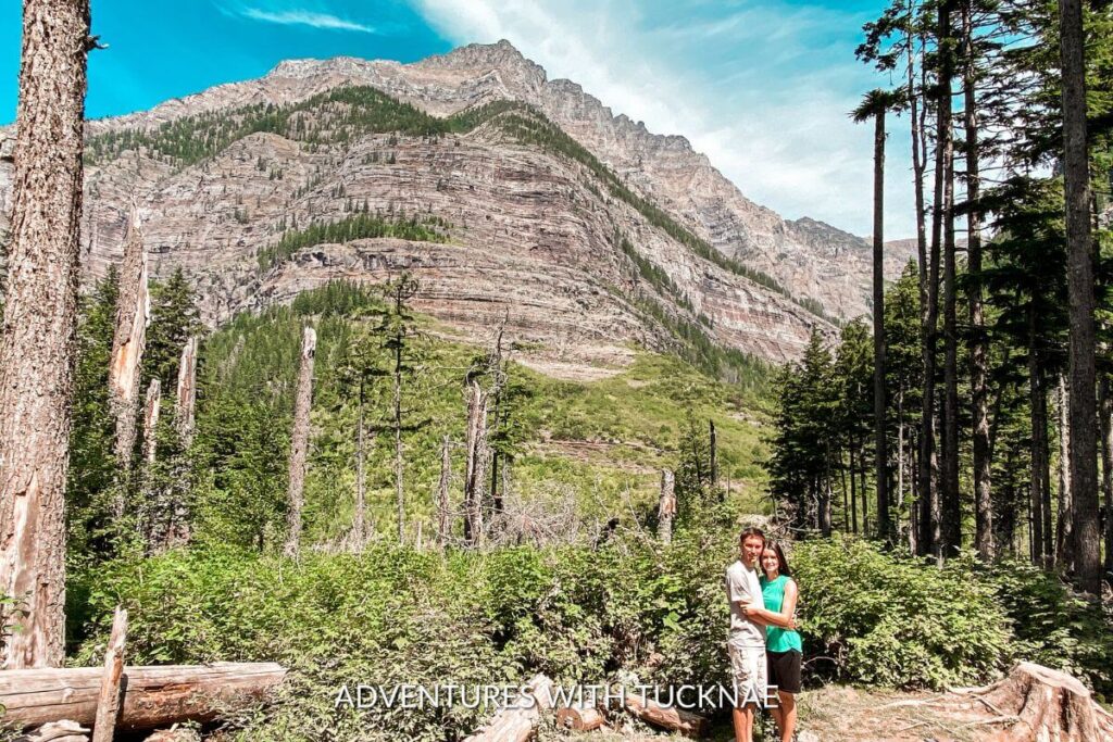 Couple hiking in Glacier National Park. They are posed on a trail with a rugged mountain behind them.