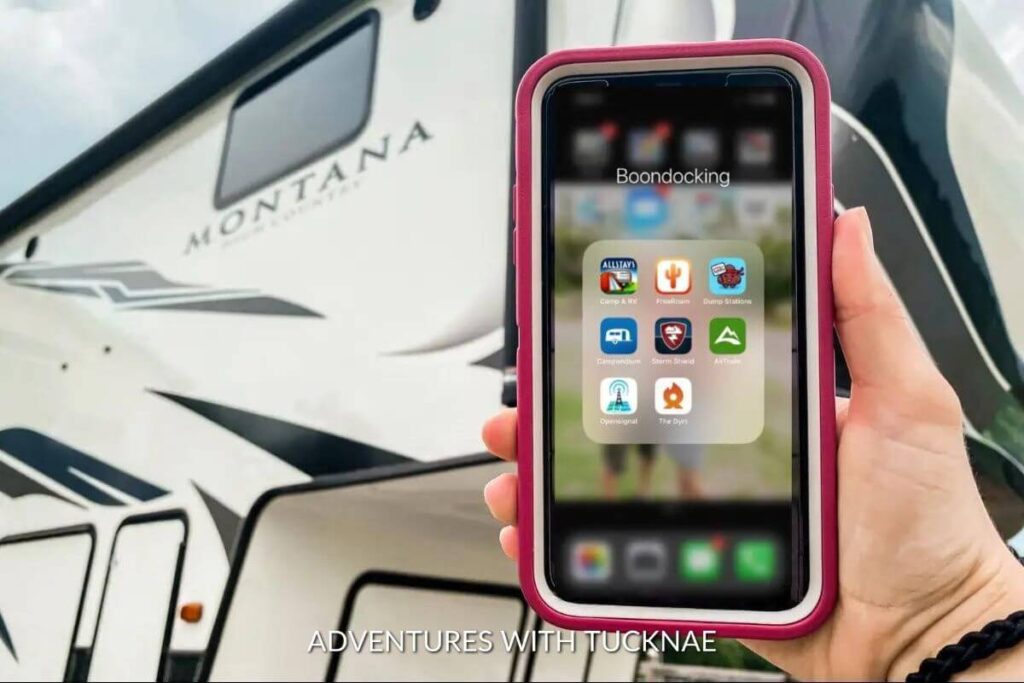 A pink phone is being held up with an RV in the background. The phone is showing a folder of apps labeled boondocking.