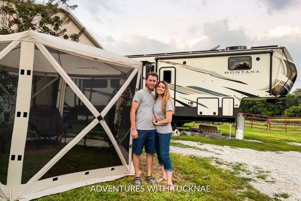 A couple is standing beside a camping gazebo with their Montana High Country fifth-wheel RV in the background.