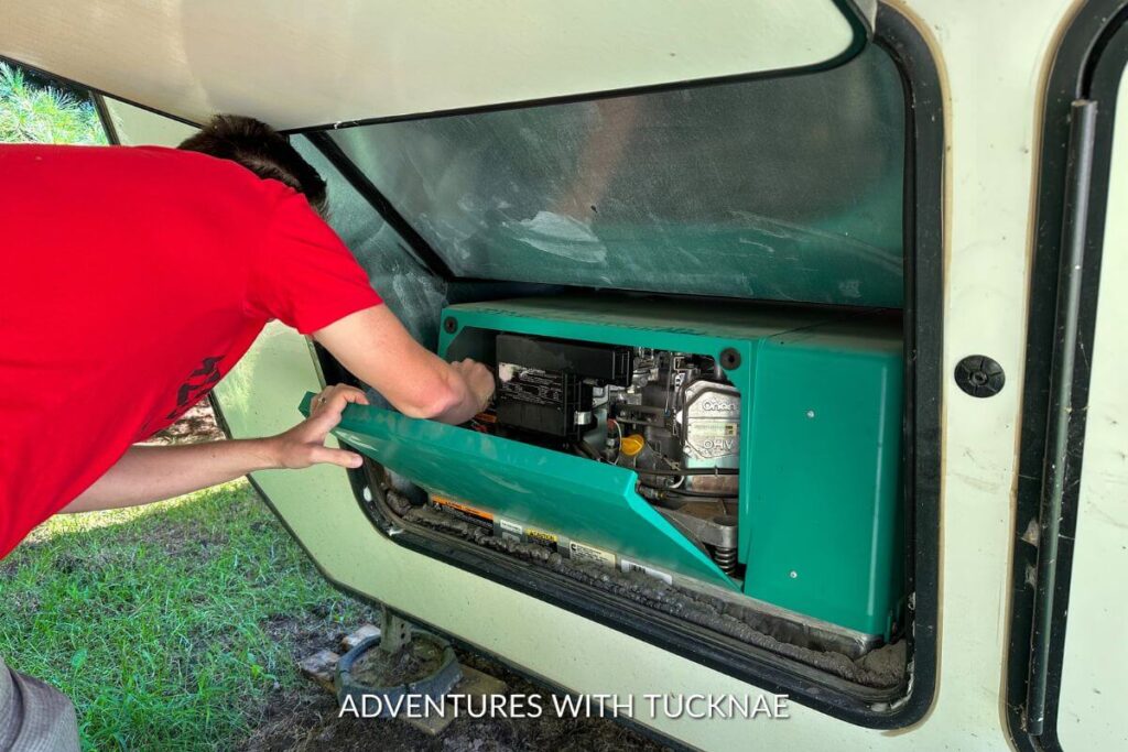 A man is starting an Onan generator in the front of an RV while boondocking.