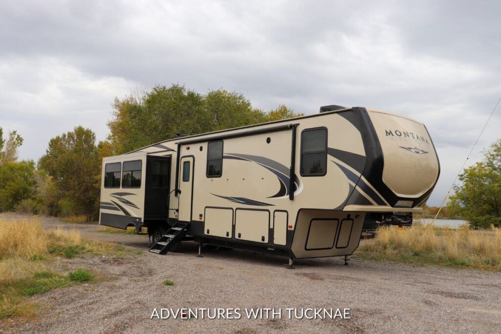 Fifth wheel RV boondocking on a gravel parking lot next to a lake.