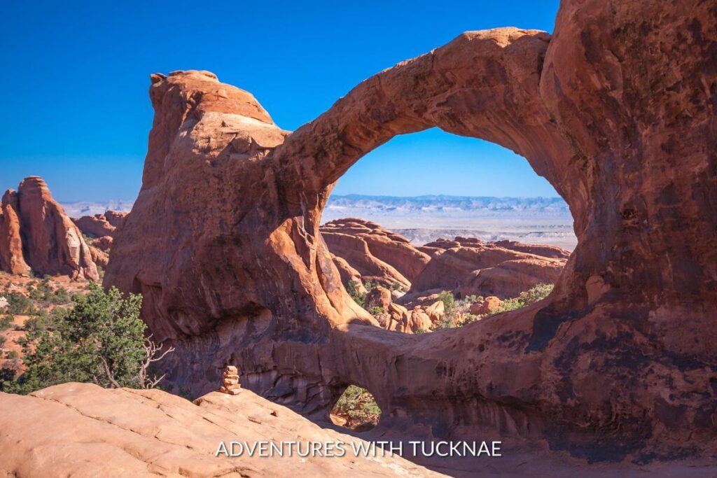 The Double O Arches in Arches National Park. The arches are made of orange sandstone and the sky is bright blue and clear. 