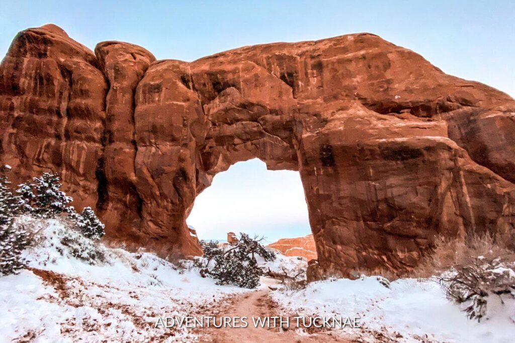 Pine Tree Arch in Arches National Park surrounded by snow on the ground. 