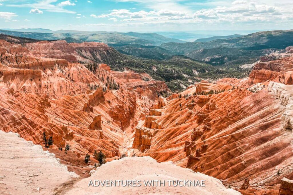 The view from above in Cedar Breaks National Monument. There are bright orange hoods all throughout the cliffs and the sky is partially cloudy and blue