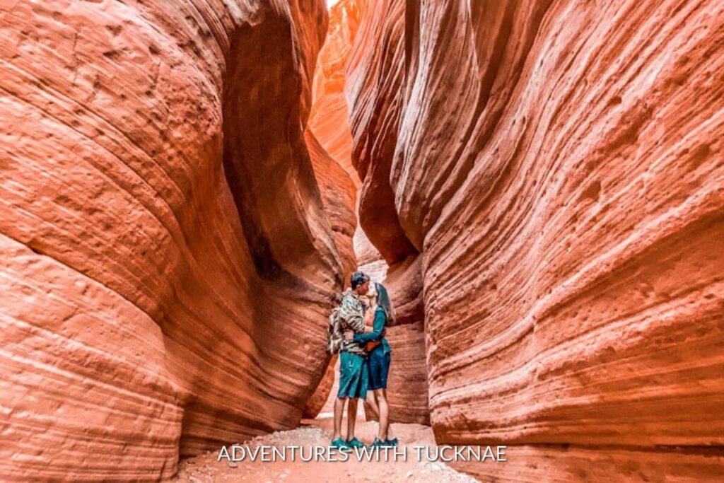 A couple standing in the center of Peekaboo Slot Canyon kissing. The canyon walls are carved sandstone and are orange