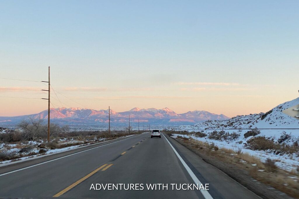 Driving in Southern Utah. The sun is setting over the mountains in the distance and there is snow on the ground.