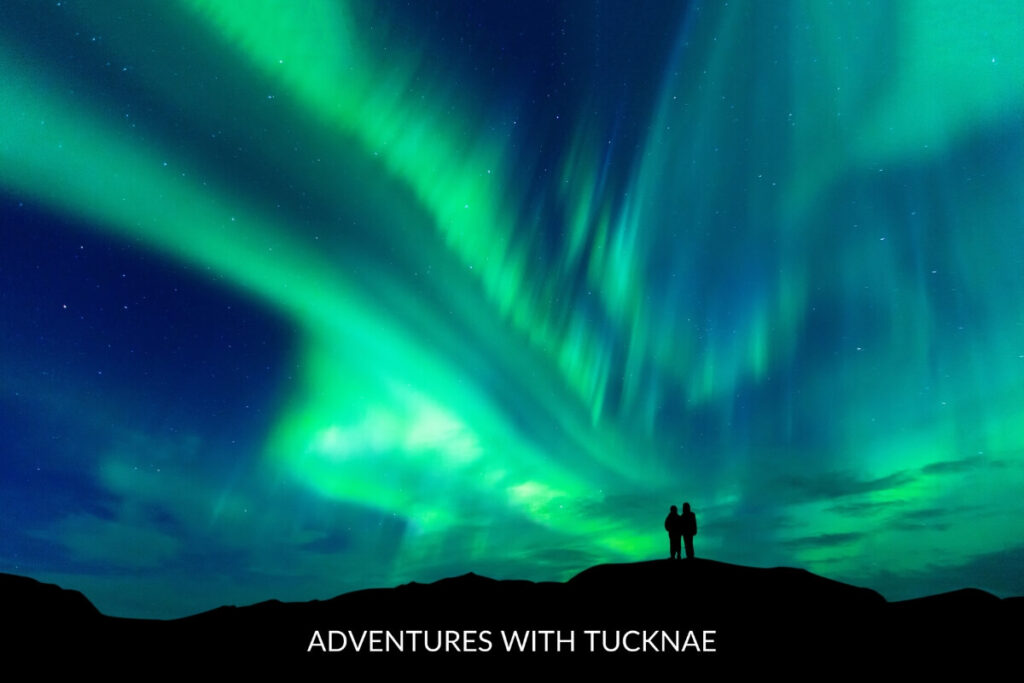 Two people standing under the bright green and blue Northern Lights in Iceland