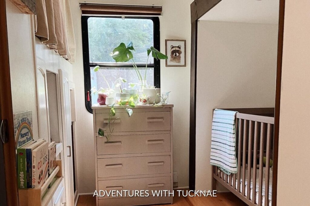 A baby crib in an RV bunk room with a dresser and plants