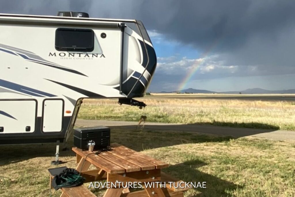 An RV with a rainbow in the distance and a Traeger grill on the picnic table