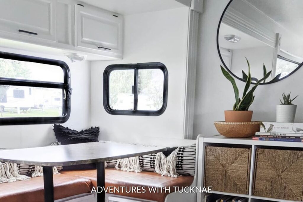 A simple white and black RV renovation featuring the dining room area with clean accents and a round mirror