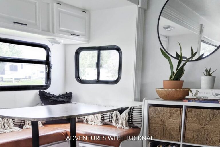 A simple white and black RV renovation featuring the dining room area with clean accents and a round mirror