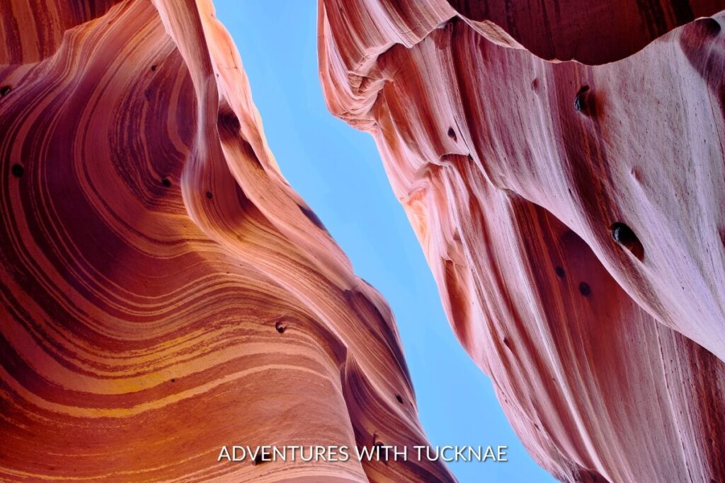 The distinct striped patterns of Zebra Slot Canyon rise vertically, a natural tapestry of orange and cream-colored rock under a brilliant blue sky.