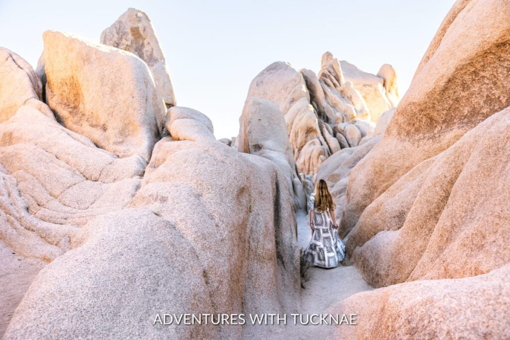 A hiker walking through the natural Arch Rock formation during a golden hour, a highlight on the Arch Rock Trail, part of the bucket list national park hikes in Joshua Tree National Park.