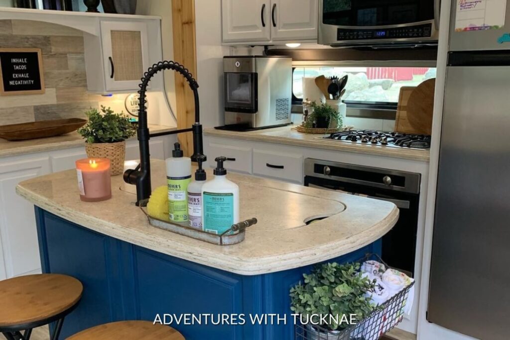 A cozy RV kitchen corner with a curved blue counter and a lit candle, with a backdrop of white cabinets and a microwave above the gas stove.