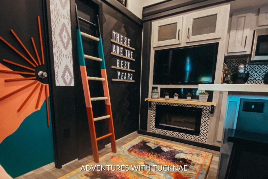 An eclectic RV interior corner with an orange and turquoise themed bunk bed ladder, a bohemian rug, and a cozy entertainment area with inspirational quote decor.