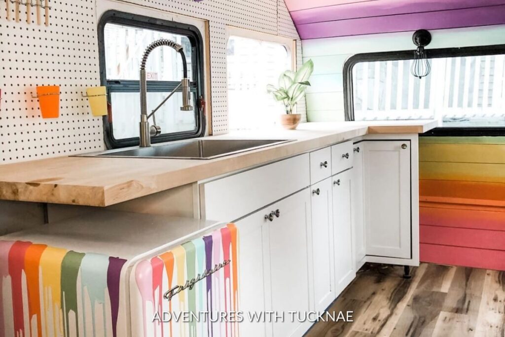 A modern RV kitchen workspace with white cabinets, a pegboard with colorful containers, and a multicolored bench, showcasing a bright and organized cooking area.