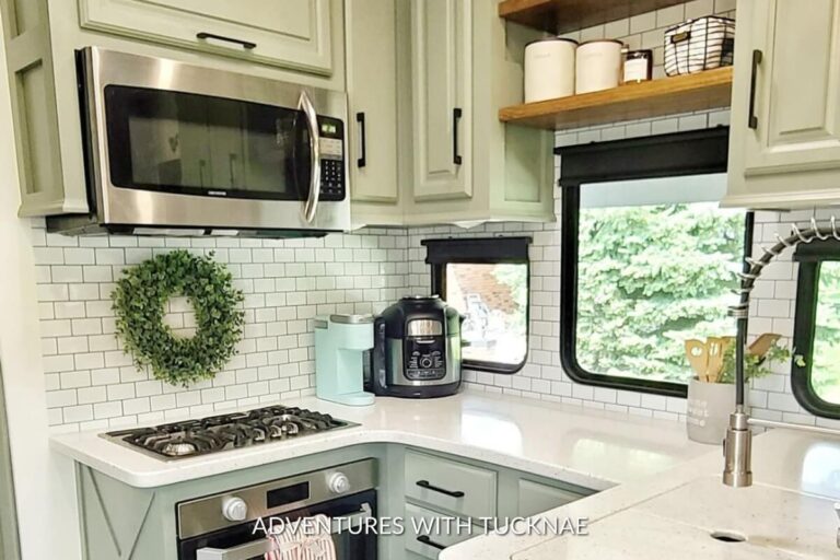 Bright RV kitchen area with white subway tile backsplash, a green wreath on the wall, stainless steel microwave above a gas stove, and a coffee maker on the counter.