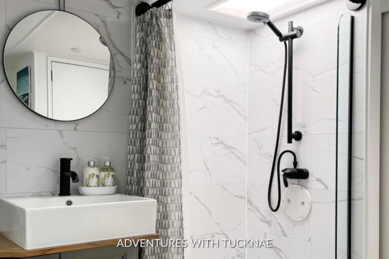 A renovated RV bathroom with carrara marble tile and a round mirror