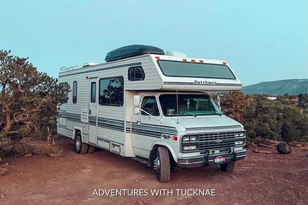 Classic Class C motorhome parked on a desert mesa with juniper trees, embodying the spirit of boondocking in a remote, scenic landscape.