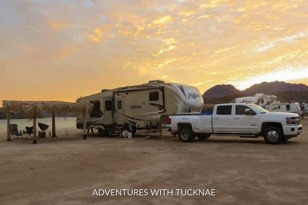 Twilight hues paint the sky as a fifth-wheel RV and pickup truck are silhouetted against a desert backdrop, illustrating a peaceful evening in a remote boondocking location.