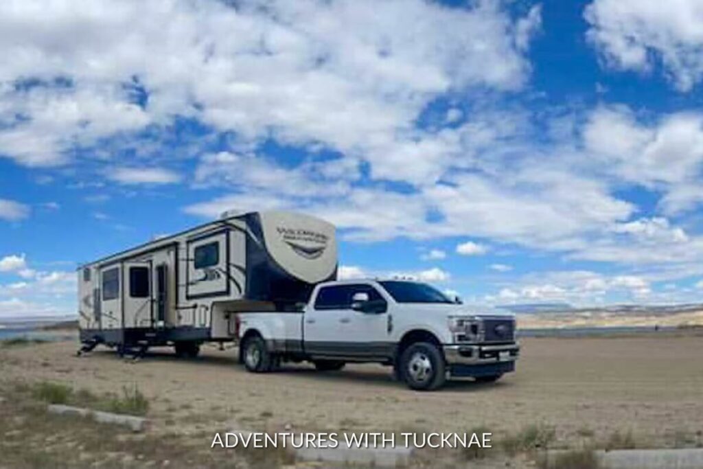 A large fifth-wheel RV attached to a white pickup truck, parked on a deserted plain under an expansive blue sky, showcasing the freedom of boondocking.