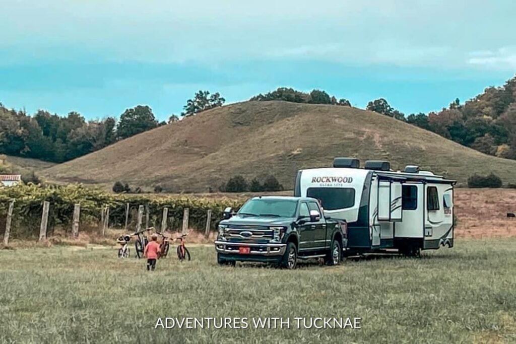 A boondocking scene in a pastoral setting, featuring a travel trailer connected to a pickup truck, with children and bicycles nearby, depicting family boondocking adventures.