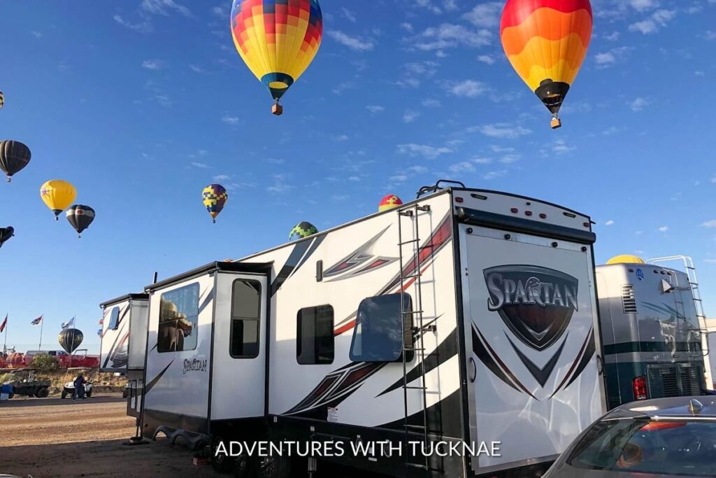 Hot air balloons rise in the morning sky behind an RV parked for boondocking at a balloon festival, capturing the adventurous spirit of RV living.