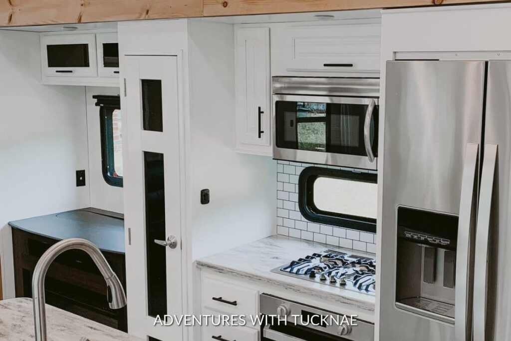 Minimalist RV kitchen with sleek white cabinetry, a microwave, and a stainless steel refrigerator beside a marble countertop.