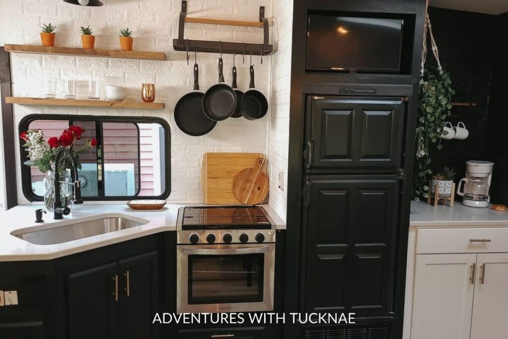 Modern RV kitchen with black countertops, floating wooden shelves with pots, and a white subway tile backsplash.