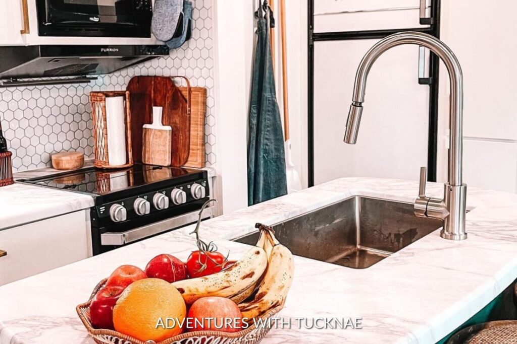 Compact RV kitchen corner with hexagon tile backsplash, a steel sink filled with fresh produce, and a cutting board.