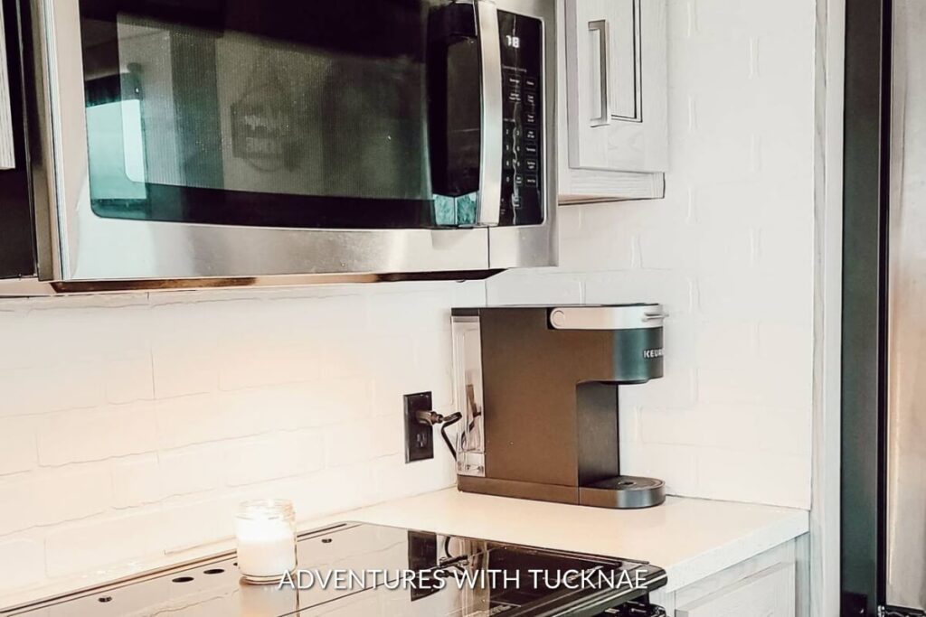 Simplistic RV kitchenette featuring a microwave, a single-serve coffee maker, and a clean white brick-style backsplash.