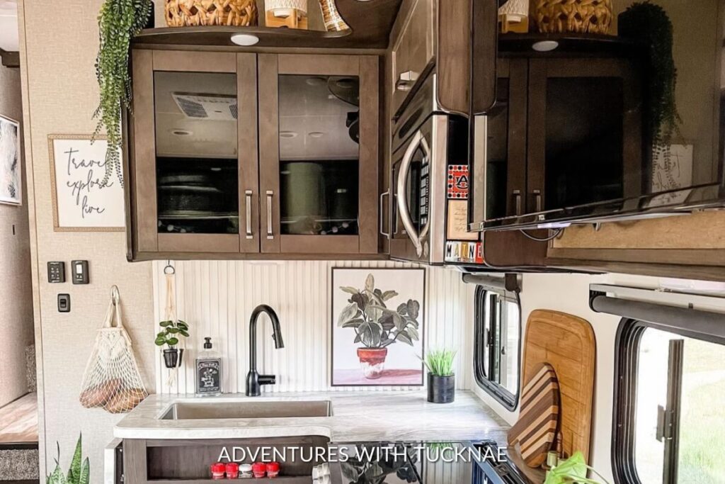 Homely RV kitchen with dark cabinets, a metal sink, a framed quote on the wall, and a plant adding a touch of greenery.