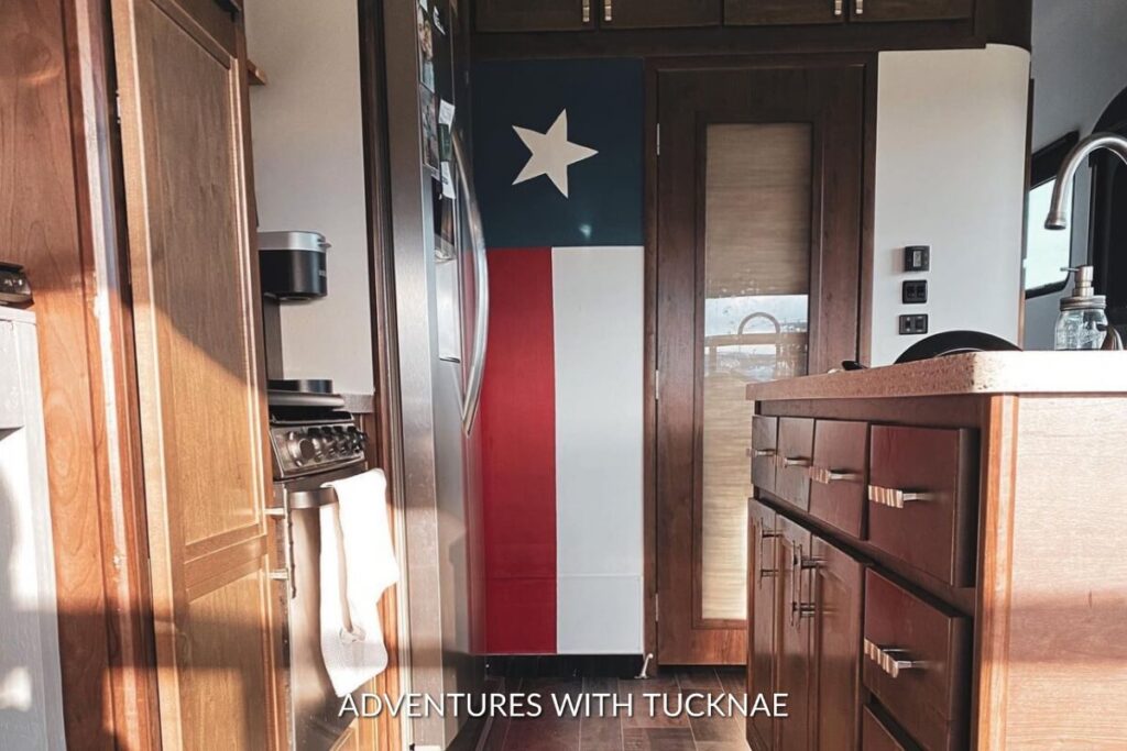 Sleek kitchen area in an RV with a Texas flag design on a vertical panel, surrounded by rich wooden cabinetry.