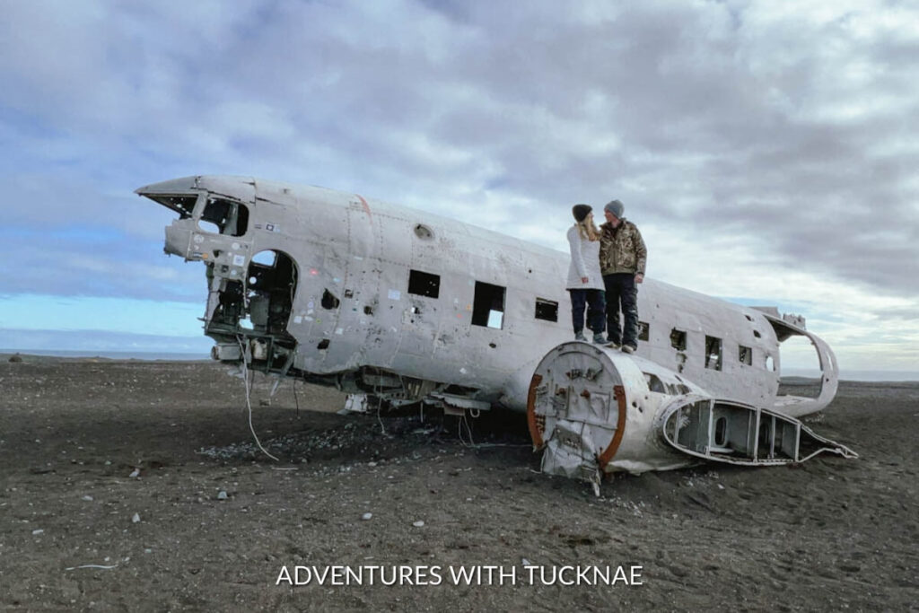 A couple standing on the wing of the DC3 plane wreck in Iceland