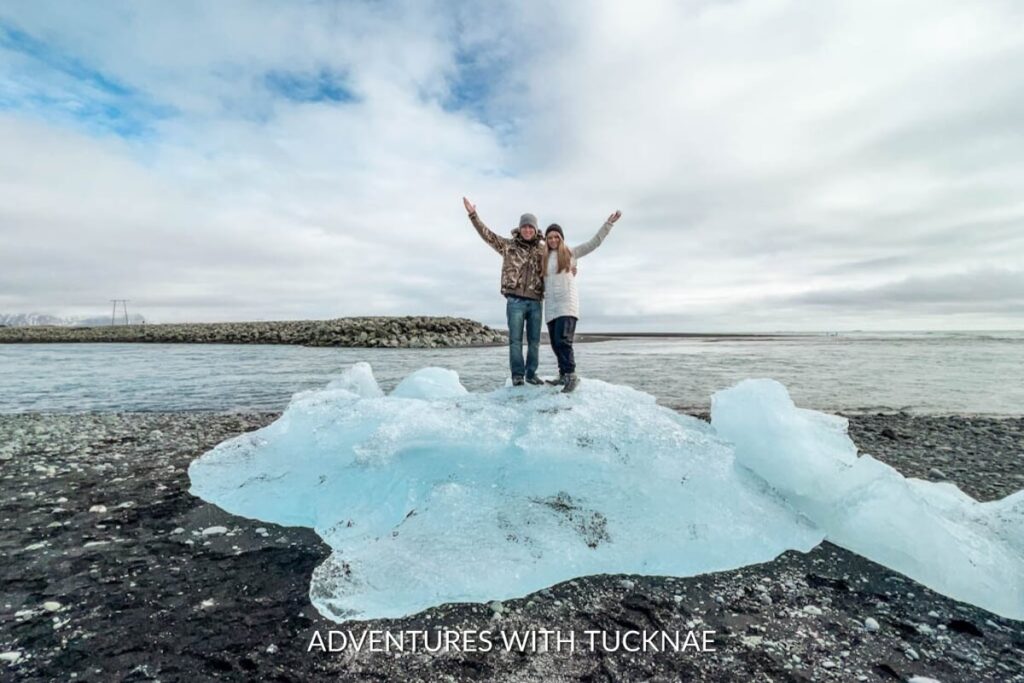 A couple standing on a chunk of ice at Diamond Beach in Iceland