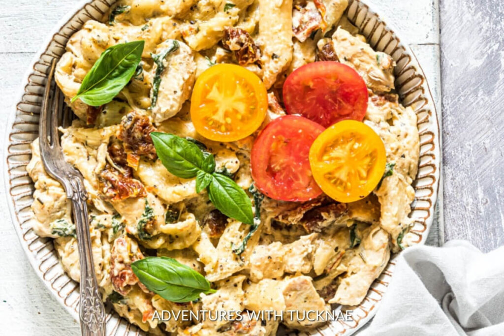 A creamy serving of RV camping crockpot meal featuring Tuscan chicken pasta with sun-dried tomatoes and fresh basil.