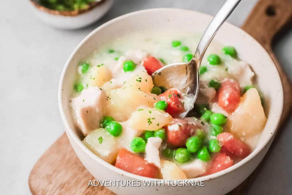 Hearty bowl of chicken pot pie soup, a perfect crockpot meal for RV camping, with tender chicken chunks, peas, and carrots.