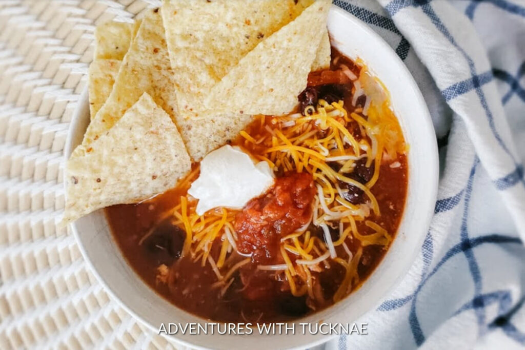A bowl of rich chicken tortilla soup topped with shredded cheese and tortilla chips, a classic rv camping crockpot recipe for warm comfort.